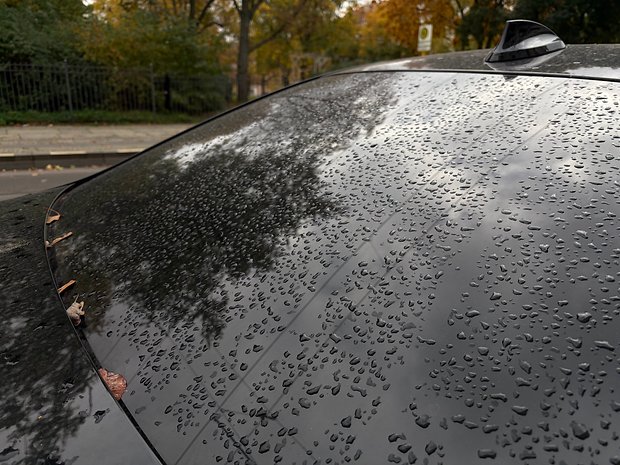 Nahaufnahme eines nassen Autofensters mit Wassertropfen und einigen gefallenen Blättern.