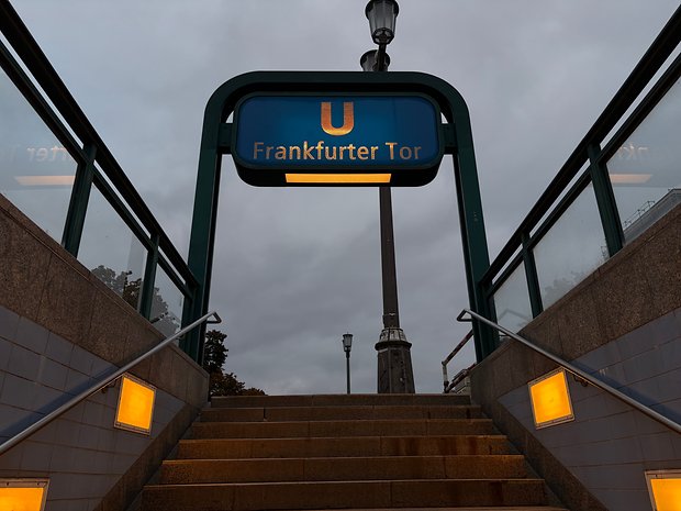 Schild der U-Bahn-Station Frankfurter Tor mit wolkigem Himmel und Treppe, die nach oben führt.