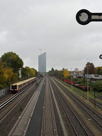 Eisenbahnschienen führen zu einem Bahnhof mit einem Gebäude im Hintergrund unter einem bewölkten Himmel.