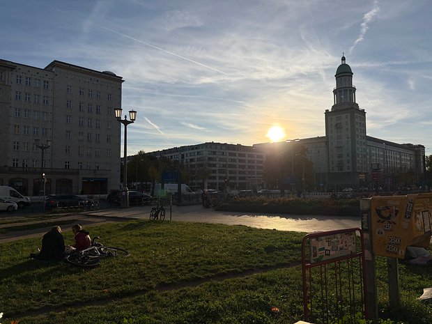 Sonnenuntergang über einer Stadtlandschaft mit Menschen auf dem Gras, Fahrrädern in der Nähe.