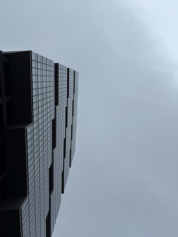 Ein hoher Gebäudekomplex mit Glasfassade vor einem bewölkten Himmel.