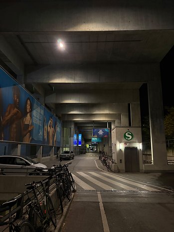 Ein schwach beleuchteter urbaner Durchgang mit Postern an den Betonwänden und geparkten Fahrrädern an der Seite.