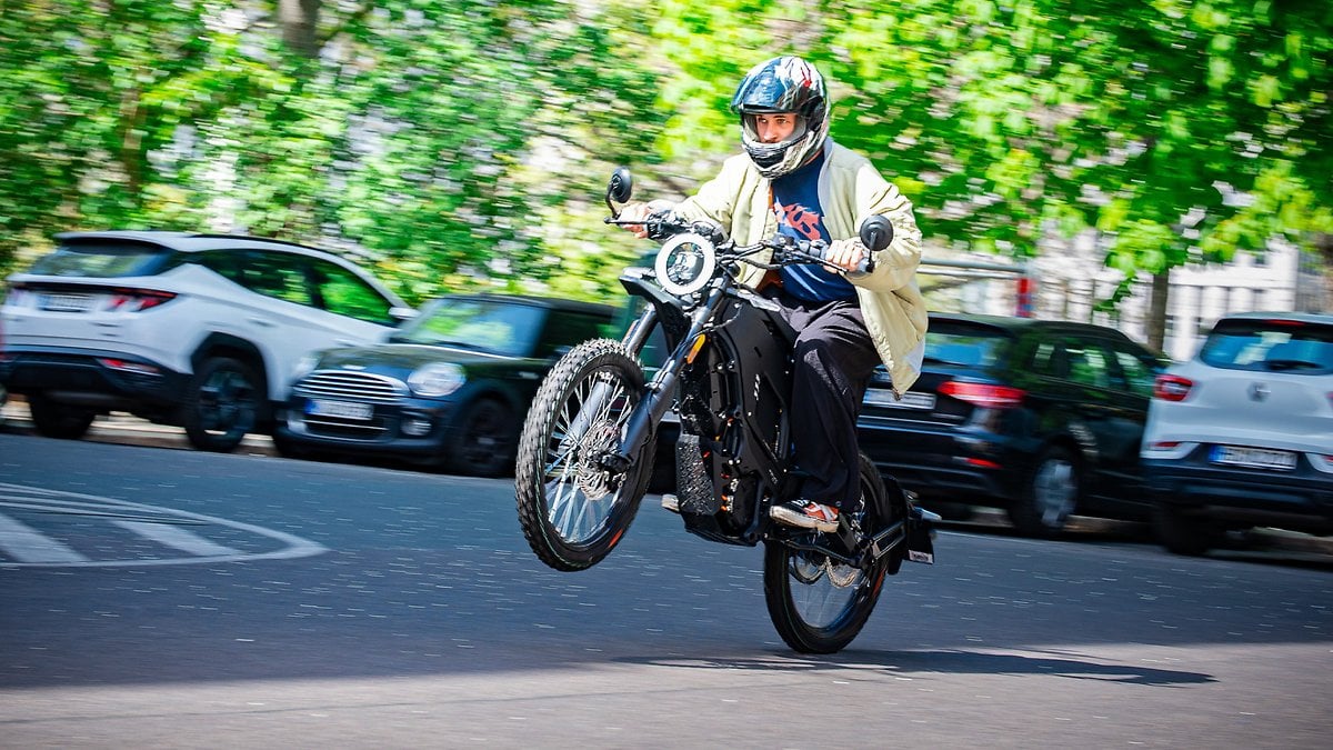 Une personne roulant sur une moto effectuant un wheeling sur une rue bordée de voitures garées.
