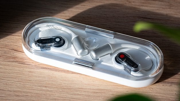 A pair of Nothing Ear (open) wireless earbuds in a clear case on a wooden surface.