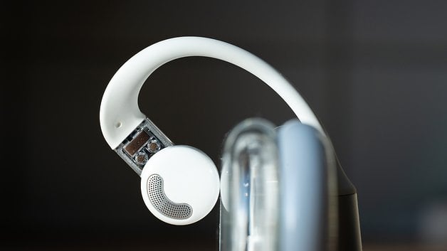 A closeup of a white earbud with a unique design against a dark background.