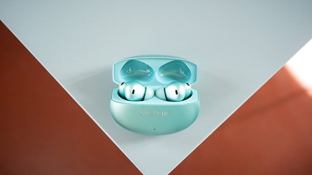 Ein Paar OnePlus Buds 4 in ihrem Ladeetui, auf einer hellen Oberfläche präsentiert.