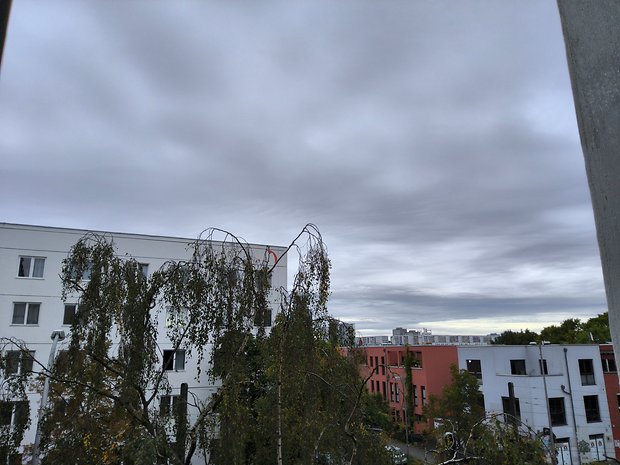 Bewölkter Himmel über Gebäuden mit Bäumen im Vordergrund.