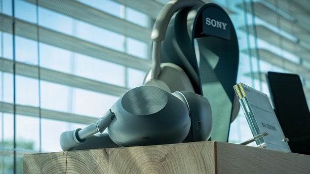 Sony WH-1000XM6 headphones on a wooden surface next to a window.