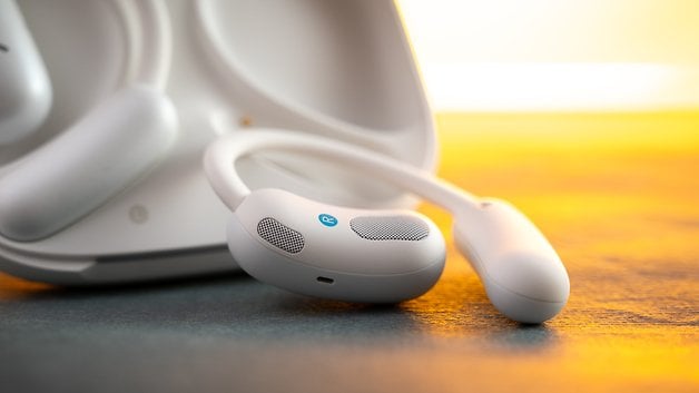 Close up of Soundcore Aerofit 2 wireless earbuds on a surface with a warm, glowing background.