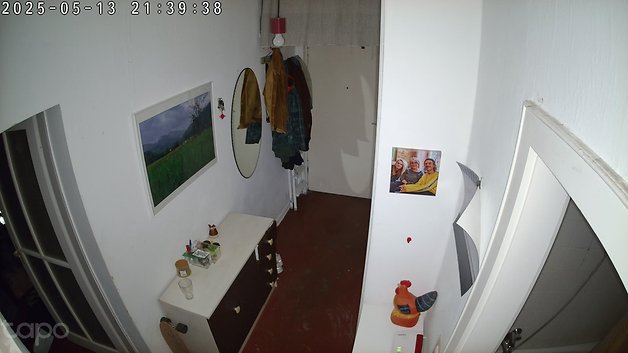 Ein Flur mit einem Spiegel, Wandkunst, hängenden Mänteln und einem Foto von drei Personen. Zeitstempel: 2025-05-13 21:39:38.