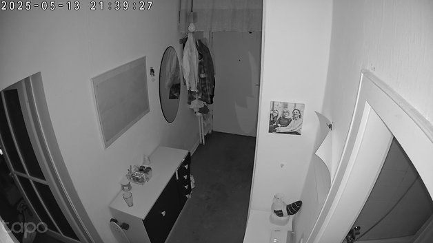 Ein schummriger Flur mit einem Spiegel, hängenden Kleidungsstücken und einem Foto an der Wand.