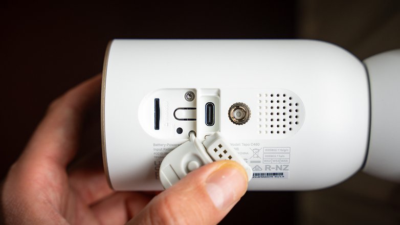 Nahaufnahme der Rückseite des Tapo C460 Geräts mit Anschlüssen und einer Hand, die ein Kabel hält.