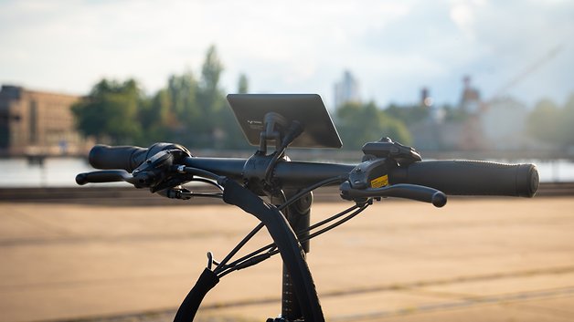 Lenker eines Fahrrads mit montiertem Display, vor einem Uferhintergrund.