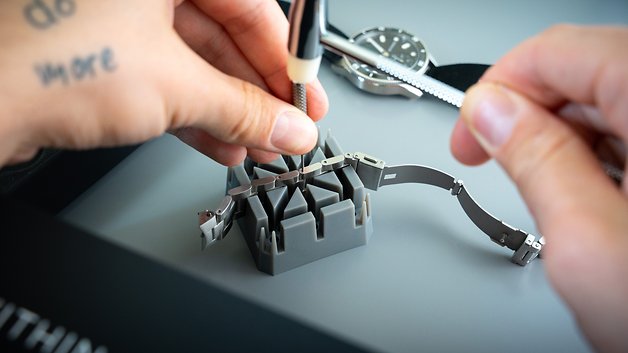 Eine Person montiert ein Withings ScanWatch Nova Uhrenarmband mit einem Werkzeug auf einer grauen Oberfläche.