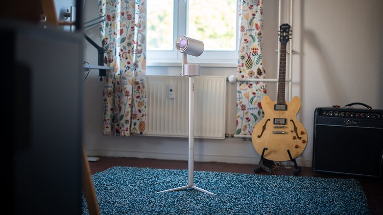 Un projecteur XGIMI MoGo 3 sur un support dans une pièce confortable avec une guitare et un amplificateur.