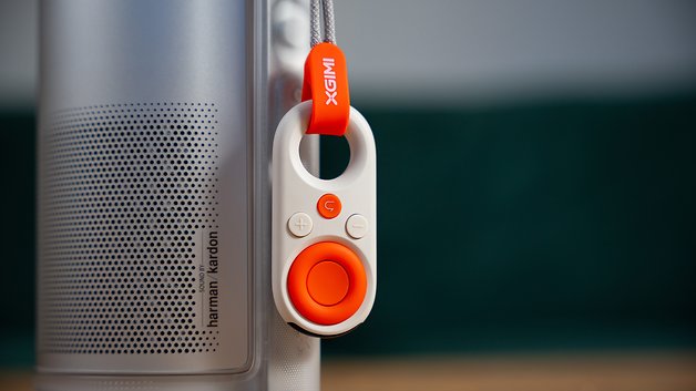 Eine Nahaufnahme einer XGIMI-Fernbedienung, die an einem Lautsprecher mit Harman Kardon-Logo befestigt ist.