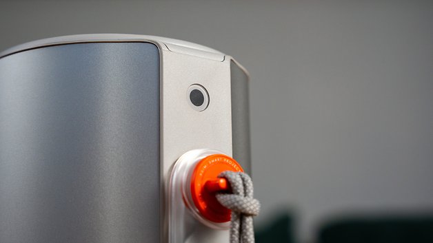 Nahaufnahme eines silbernen Geräts mit einem Objektiv und einem orangefarbenen Knopf, der an einem Seil befestigt ist.