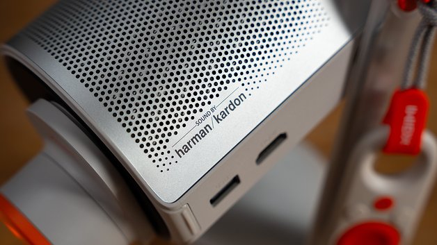 Nahaufnahme eines silbernen Lautsprechers mit durchbrochener Oberfläche, beschriftet mit 'sound by harman/kardon'.