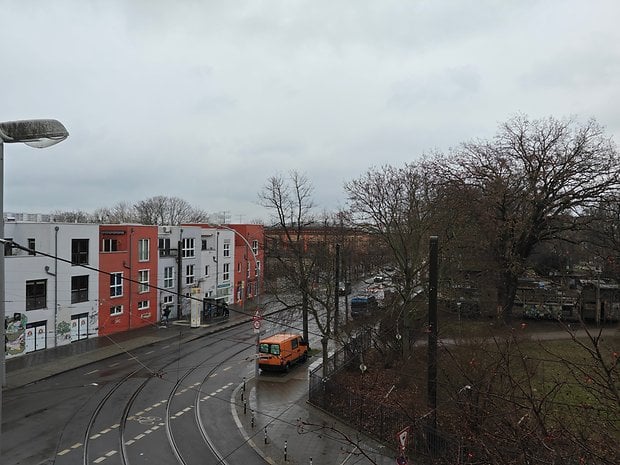 A rainy street view with colorful buildings, an orange pickup truck, and bare trees on a cloudy day.