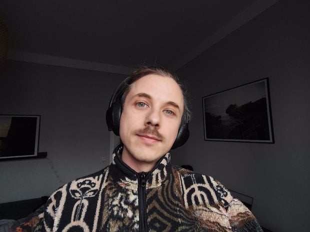 A person wearing headphones smiles at the camera while wearing a patterned fleece jacket.