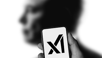 Ein verschwommener Elon Musk hinter einem Smartphone mit xAI-Logo