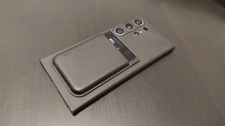 A smartphone with a black leather case placed on a textured surface.