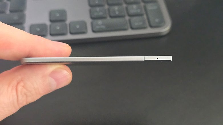 A person holding a slim, silver device with a small hole on one end, background shows a keyboard.