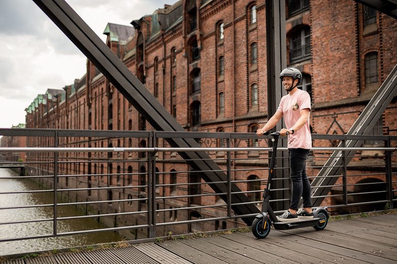 Mann fährt den E-Scooter auf einer Brücke