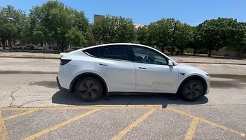 Ein weißes Tesla Model Y, das auf einem Parkplatz steht, mit Bäumen im Hintergrund.