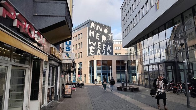 Eine Straßenansicht mit Gebäuden und einem Wandgemälde, das 'ANOTHER WEEK' liest.