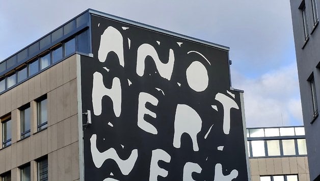 Un mur de bâtiment avec de grandes lettres blanches disant 'ANOTHER WEEK'.