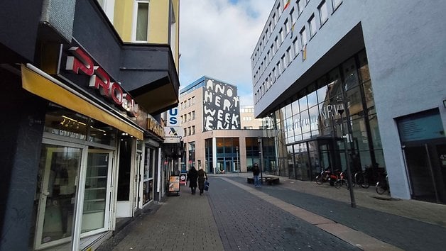 Eine Straßenansicht mit Geschäften und einem Gebäude mit Graffiti, das 'ANOTHER WEEK' liest.