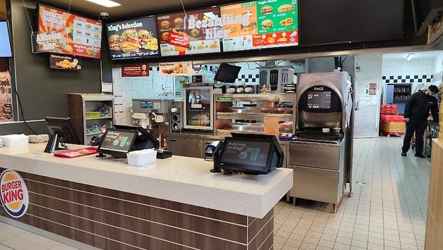 Comptoir Burger King avec écrans de menu, bornes de commande et zone de préparation des aliments.