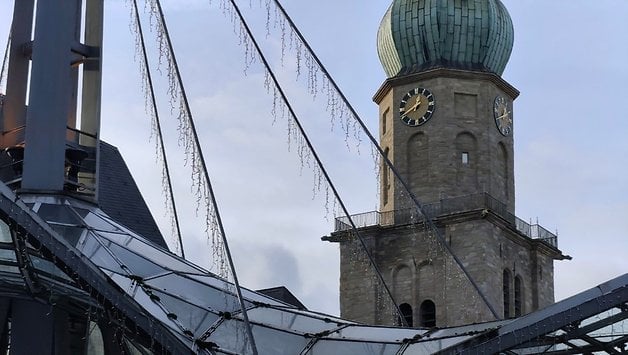 Ein Uhrturm mit einer grünen Kuppel, umgeben von moderner Architektur und dekorativer Beleuchtung.