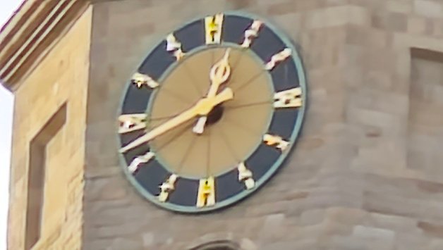 Gros plan d'une horloge de tour avec des marqueurs d'heure ornés et des aiguilles.