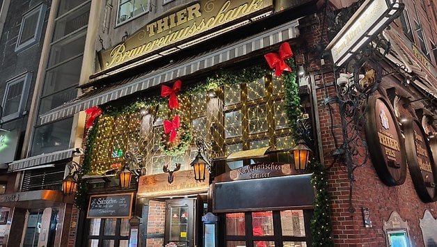 Eine dekorierte Pub-Fassade mit Weihnachtslichtern und Schleifen, die den Namen 'THIER Brauereiwirtschaft' trägt.