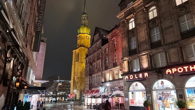 Eine regnerische Nachtansicht einer Straße mit historischen Gebäuden und einem Uhrturm.