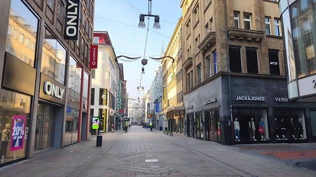 Une rue commerçante calme avec des magasins fermés, dont ONLY et JACK & JONES, par une journée ensoleillée.