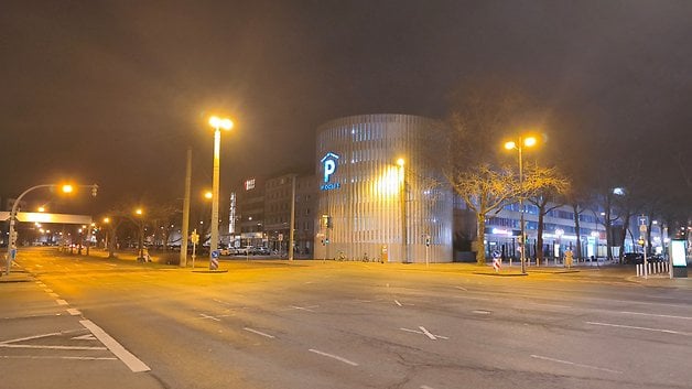 Une rue calme la nuit avec des arbres illuminés et un bâtiment moderne affichant un panneau 'P'.