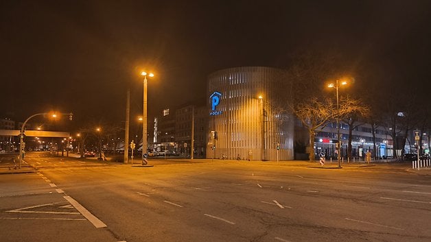 Eine schwach beleuchtete Straße bei Nacht mit einem Parkhaus und beleuchteten Straßenlaternen.