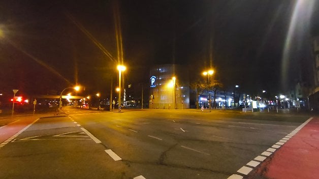 Scène urbaine nocturne avec des lampadaires illuminant une route presque vide et un bâtiment avec un panneau de stationnement.