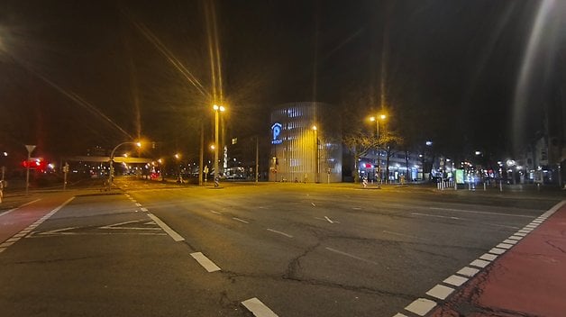 Rue de la ville la nuit avec des bâtiments illuminés et une route vide.