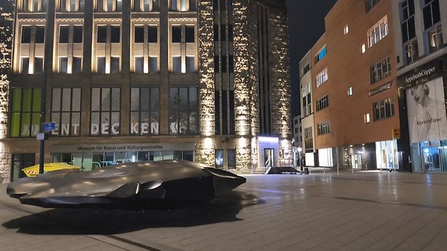 Eine moderne Skulptur vor einem Museumsgebäude bei Nacht, mit beleuchteter Architektur.