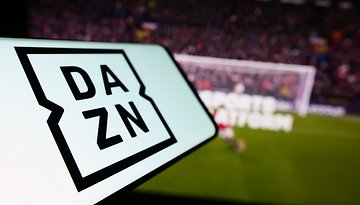 DAZN-Logo auf einem Handy und ein Fußballstadion im Hintergrund