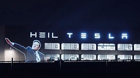 Eine Projektion einer Person mit dem Text 'HEIL TESLA' auf einem Gebäude bei Nacht.