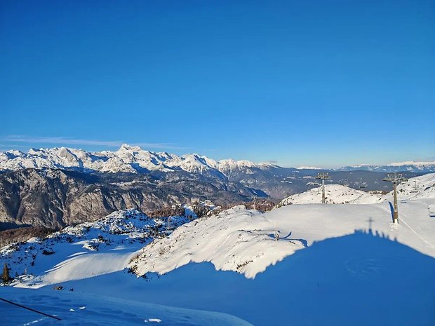 Montanhas cobertas de neve sob um céu azul claro com teleféricos em primeiro plano.