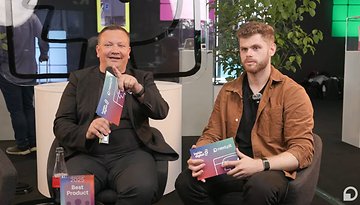 Zwei Männer sitzen in Stühlen auf der IFA, halten Auszeichnungen und diskutieren, mit Pflanzen im Hintergrund.
