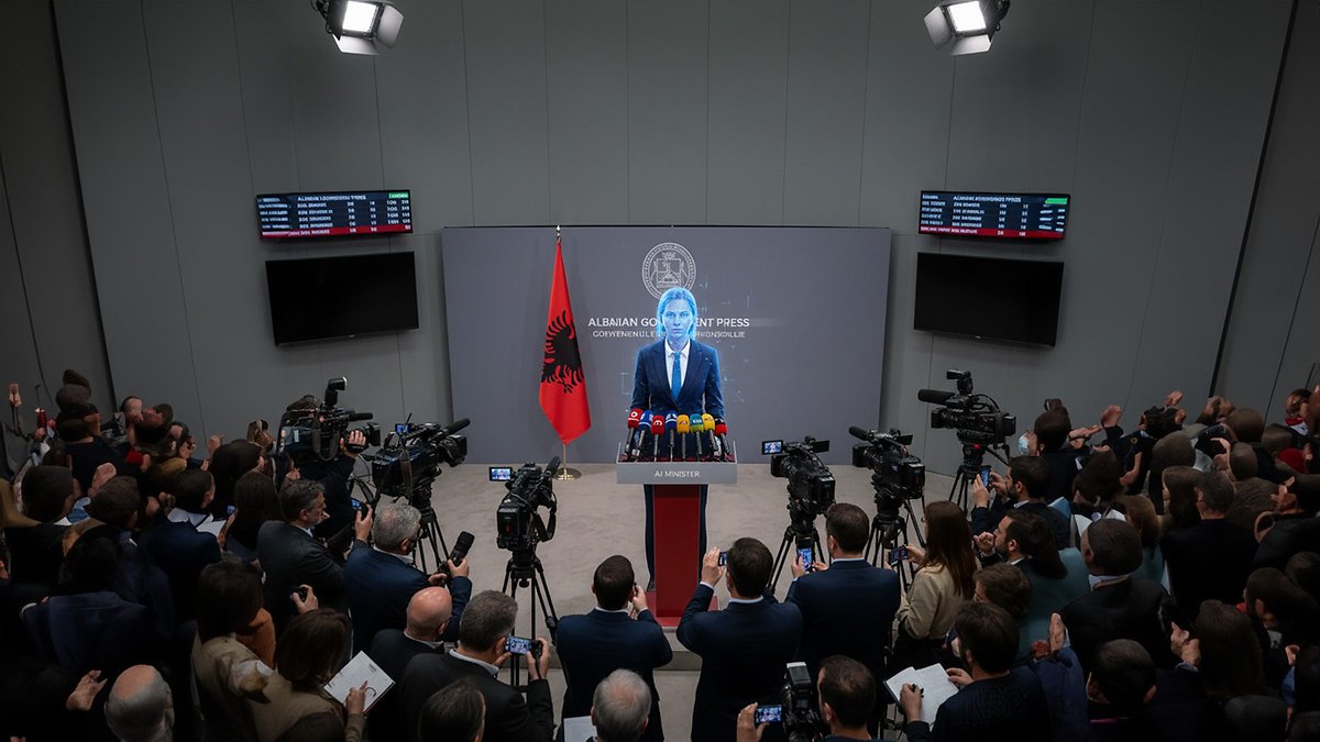 Une conférence de presse en Albanie avec un intervenant au pupitre, entouré de caméras et d'un drapeau albanais.
