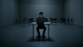 Eine Person sitzt allein an einem Tisch mit einem Laptop in einem dunklen, leeren Raum.