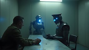 Ein humanoider Roboter verhört einen Mann in einem schwach beleuchteten Raum, während ein anderer Roboter daneben steht.